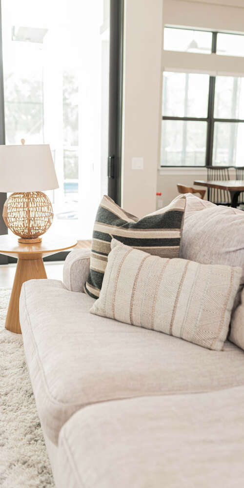 White Sofa next to white lamp on top of wood small table and large window