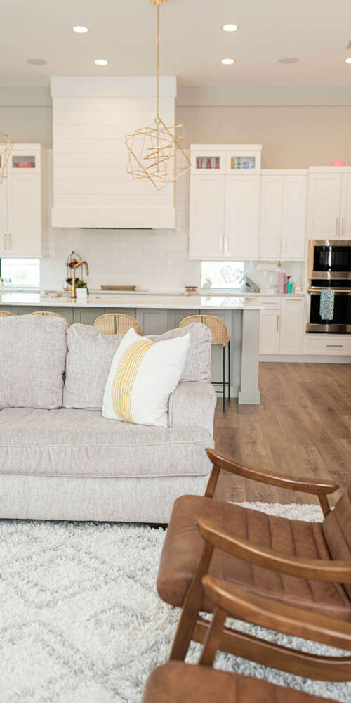 white kitchen with marble finishes next to livingroom with white sofa and leather chers with wood floor