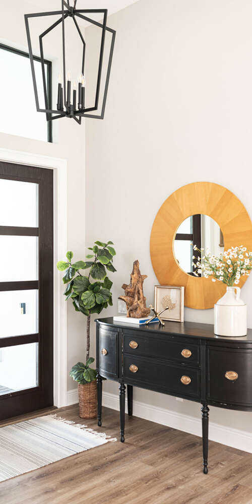 dark wood with tempered glass windows front large door next to dark wood furniture with round shape mirror on white wall