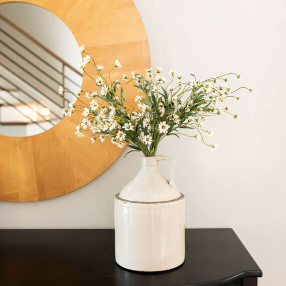 white vase with white flowers on top of dark wood table and mirror in the back