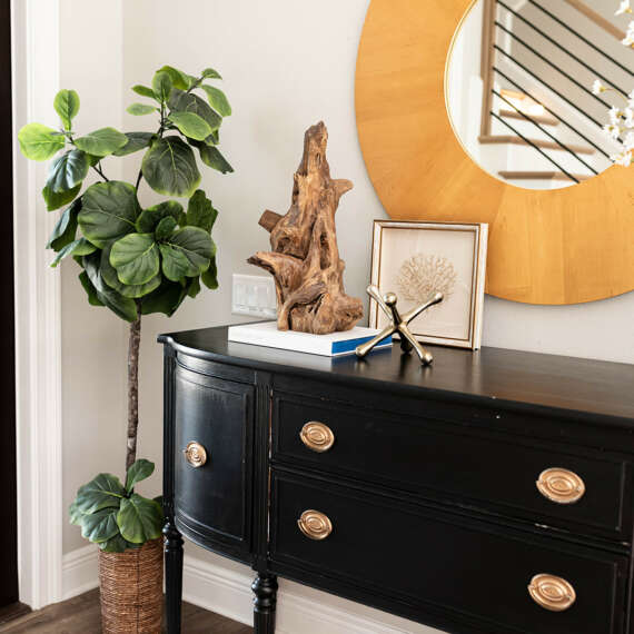 Yellow circle frame mirror with Dark wood furniture next to tall plant with wood floor