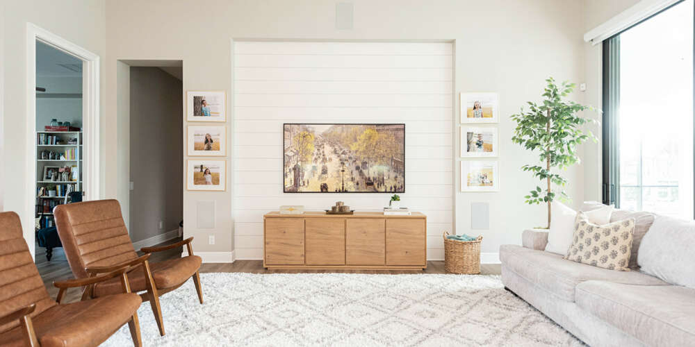 light livingroom white carpet, white cushion, two wood chairs, with tv hung on the wall