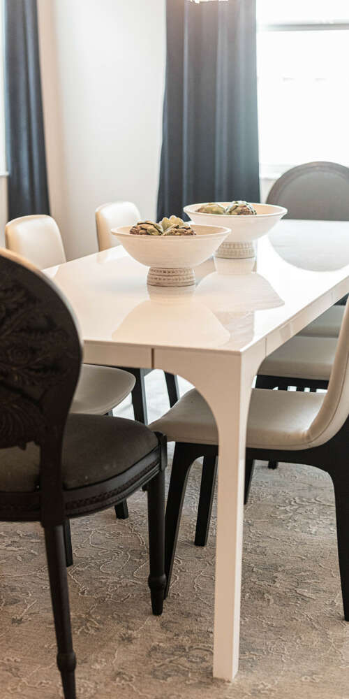 Light walls dining room-White dining table with dark chairs-dark curtains-dark furtinure-gold frame circle shape mirror-ashen wood floor-ceiling hanging lamp