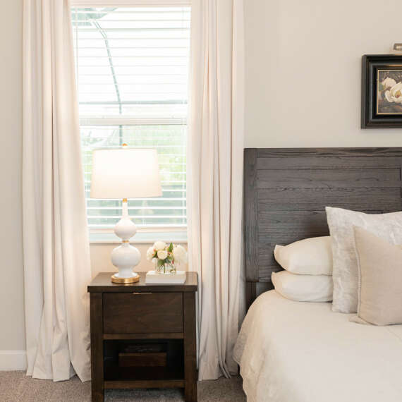 light bed layingn with dark wood bedstamp-light curtains-light wall-dark wood nightstand table
